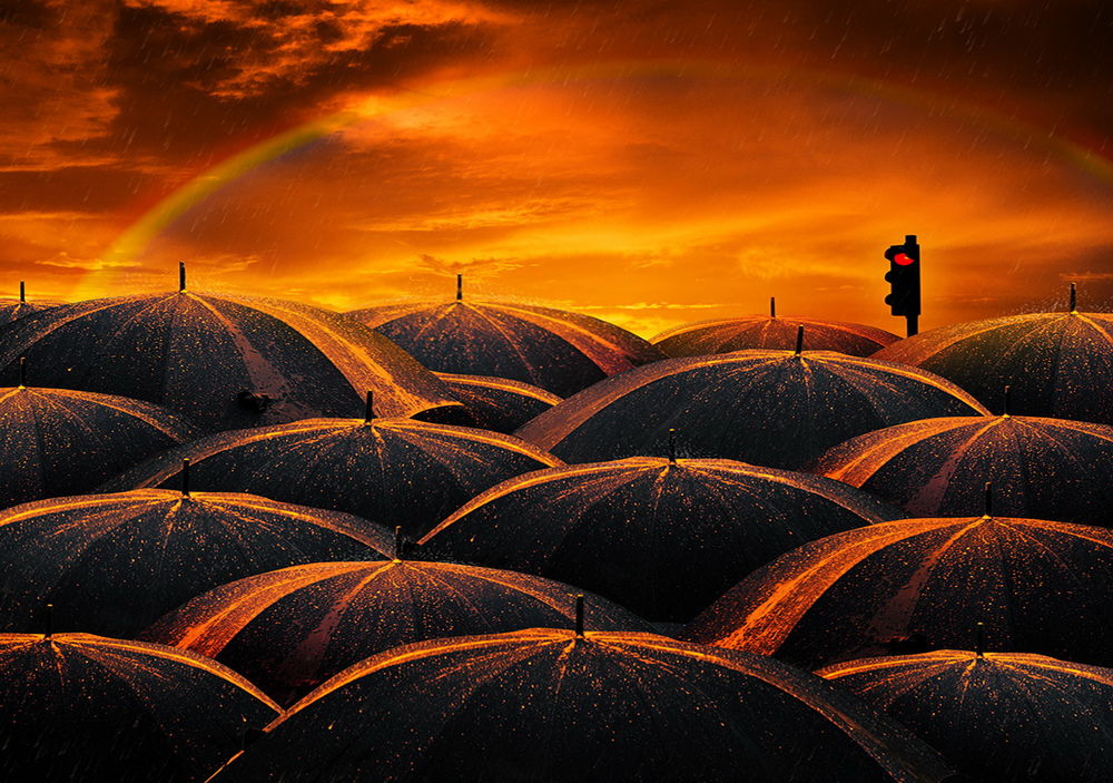 Обои для рабочего стола Множество черных зонтиков с каплями воды, освещенных багряным закатом дождевого неба с радугой, находящиеся возле светофора с включенным красным сигналом, фотография Garas lonut