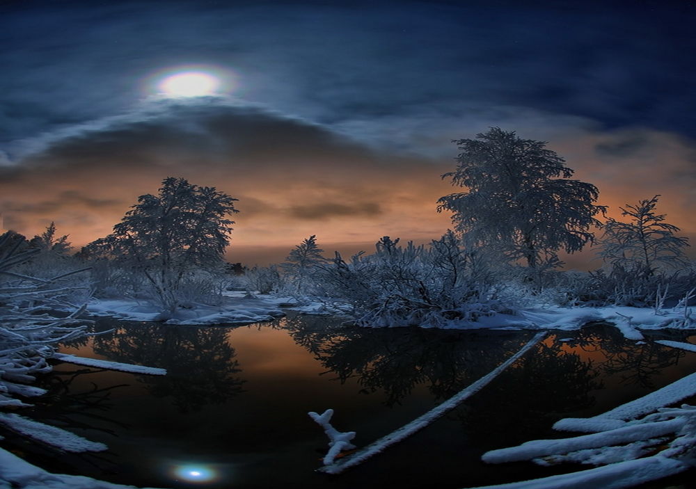 Обои для рабочего стола Небольшой незамерзающий водоем, окруженный заснеженными берегами с растущими на них деревьями на фоне ночного облачного неба с ярко светящейся луной, отражающейся в водной поверхности, фотография optimist