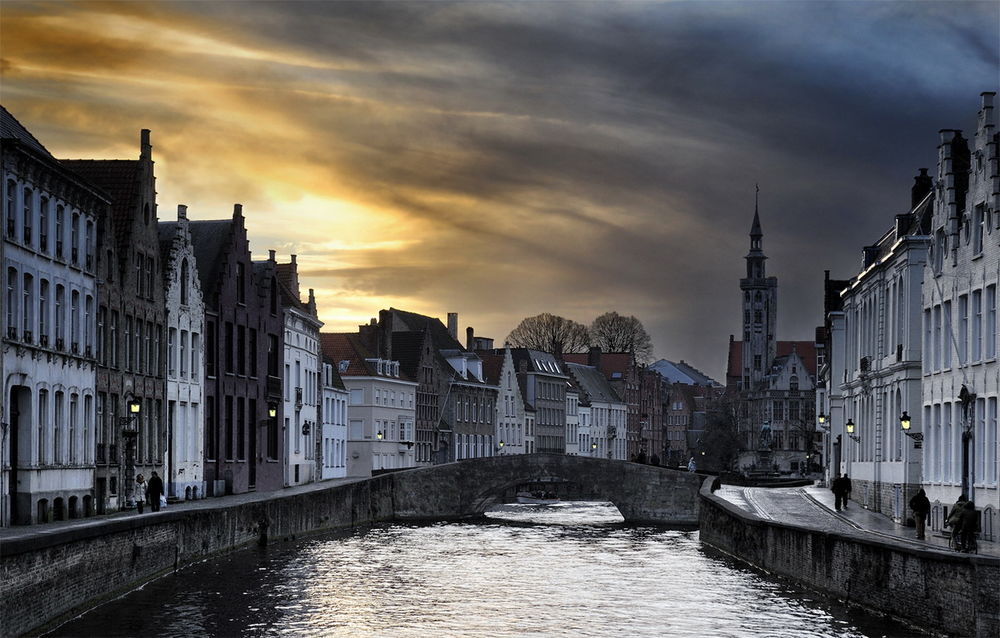 Обои для рабочего стола Набережная реки города Брюгге, Бельгия / Brugge, Belgium, на фоне заходящего солнца и темных туч на небе, фотография Danny Vengenechten