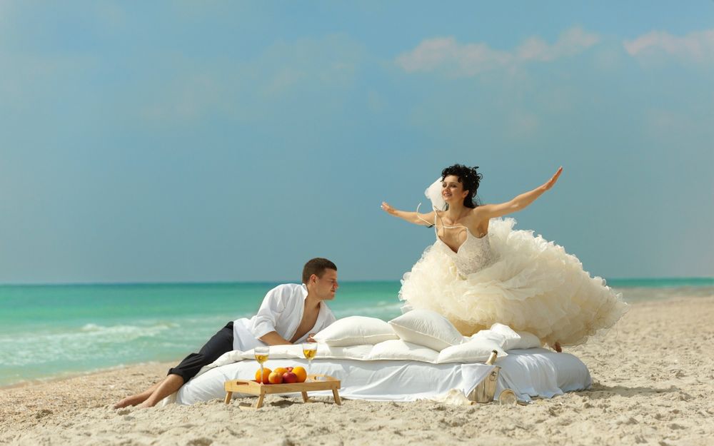 Обои для рабочего стола Невеста в пышном подвенечном платье ласточкой прыгает на брачное ложе к жениху на морском побережье