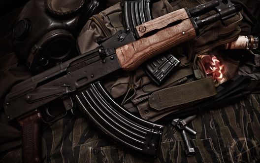 Обои на рабочий стол Автомат АК-47 лежит рядом с противогазом на камуфлированной материи