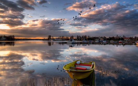 Обои на рабочий стол Лодка с комплектом весел, лежащих в ней, находящаяся на противоположном берегу озера от небольшой лодочной пристани на фоне неба с серыми кучевыми облаками и парящих птиц, фотография Эдуарда Гордеева