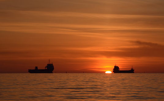 Обои на рабочий стол Две грузовые баржи, идущие по морю на линии горизонта на фоне заката солнца, фотография Румена Паисиева
