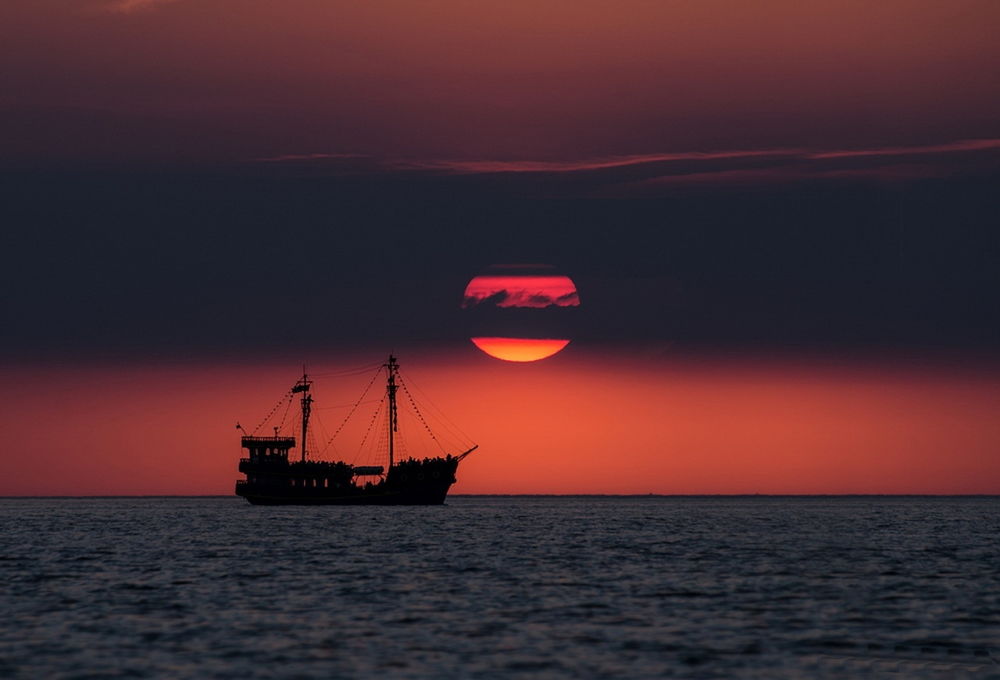 Обои для рабочего стола Морской сухогруз, идущий по морю на фоне багряного заката солнца, зашедшего за темные тучи, фотография Katarzyna Gritzmann