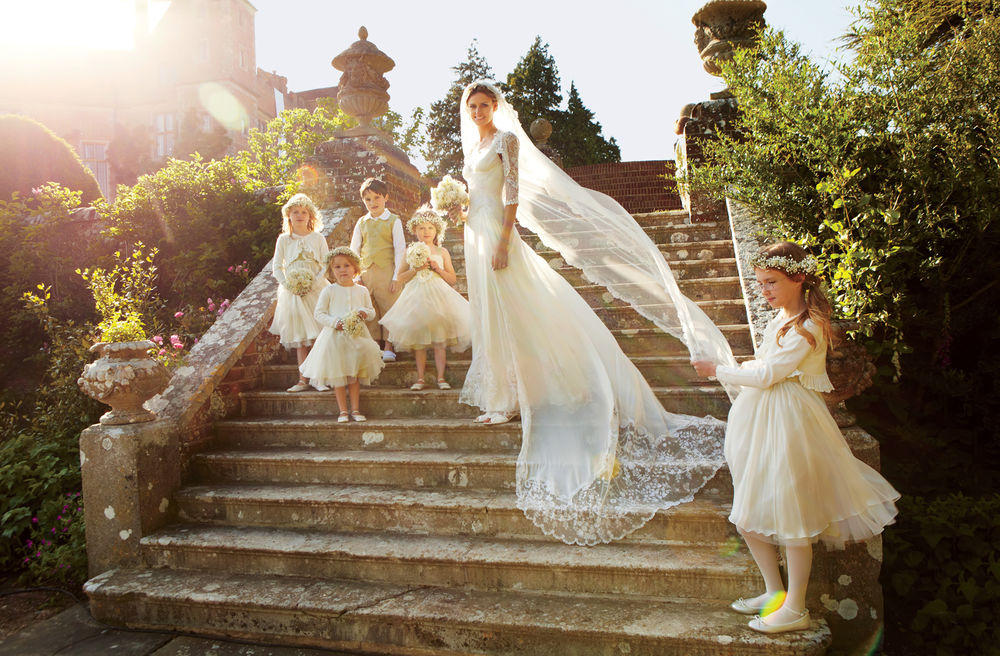 Обои для рабочего стола Британская модель Жакетта Уиллер / Jacquetta Wheeler стоит в свадебном платье на каменных ступенях в окружении детей