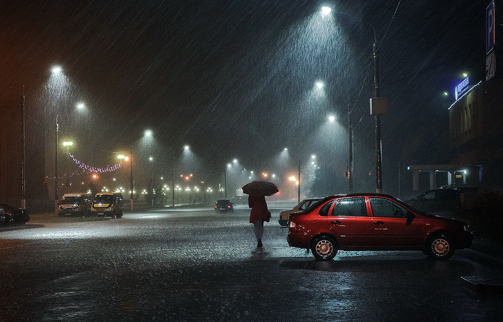 Обои для рабочего стола Одинокая девушка в красном пальто, держащая в руке зонтик, идущая по дороге ночного города под сильным ливневым дождем, фотография Александра Сысуева