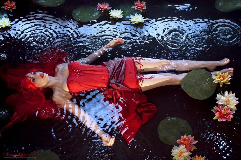 Обои для рабочего стола Девушка в красном платье лежит в воде, вокруг растут желтые, белые и розовые водяные лилии, фотограф Stefan Grosjaen / Стефан Грожан