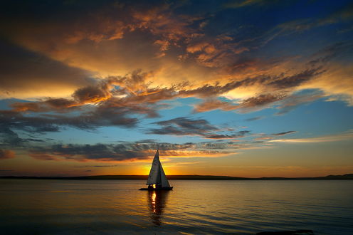 Обои на рабочий стол Парусник, плывущий по морю на фоне золотистого солнечного заката, осветившего своими лучами водную поверхность с легкой рябью, фотография Дмитрия Антипова