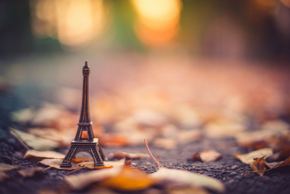 Обои для рабочего стола Статуэтка La tour Eiffel / Эйфелевой башни стоит на асфальте среди осенних листьев