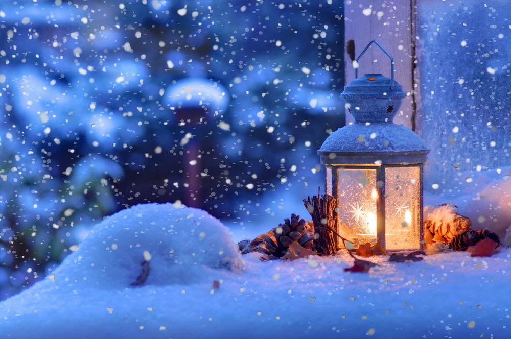 Обои для рабочего стола Фонарь с горящей свечой внутри стоит на снегу, рядом лежат еловые шишки, идет снег