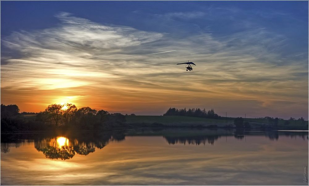 Обои для рабочего стола Дельтапланерист, парящий в воздухе над рекой на фоне заходящего за линию горизонта солнца, автор Николай Будин
