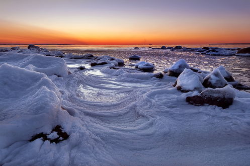 Обои на рабочий стол Сильный мороз сковал льдом прибрежные морские воды с каменистым берегом на фоне багряного заката