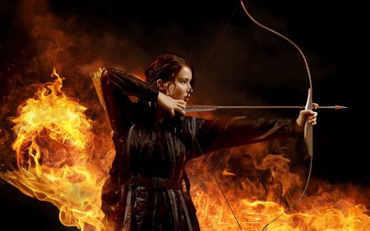 Обои на рабочий стол Дженнифер Лоуренс / Jennifer Lawrence с луком и стрелой в руках на фоне огня кадр из фильма Голодные игры / THE HUNGER GAMES