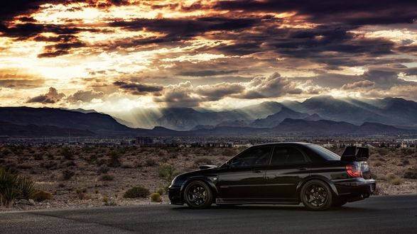 Обои на рабочий стол Subaru Impreza STI черного цвета стоит на дороге на фоне гор и облаков