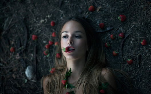 Обои на рабочий стол Девушка с клубникой во рту лежит на земле среди ягод клубники