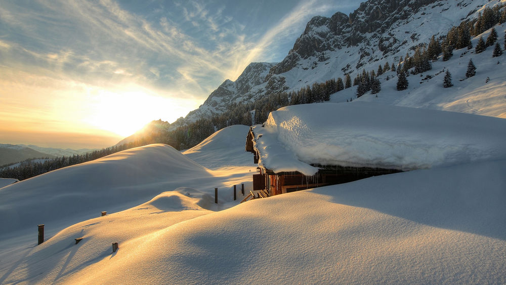 Обои для рабочего стола Восходящее из-за гор утреннее солнце на небе с перистыми облаками, осветило деревянный дом, стоящий в предгорье, засыпанный густым слоем снега