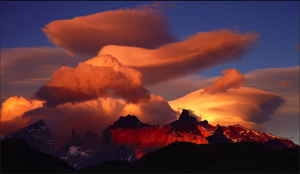 Обои для рабочего стола Необычные, красивые кучевые облака, освещенные красно-кирпичными солнечными лучами, парящие в небе над горным массивом