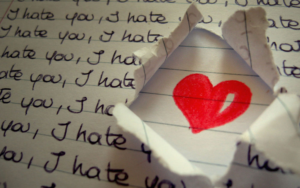 Обои для рабочего стола Тетрадь, исписанная надписями I hate you / Я тебя ненавижу, но в проделанной в бумаге дыре нарисованное сердечко