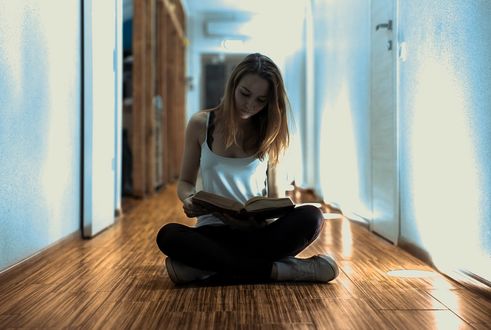 Обои на рабочий стол Девушка сидит на полу и читает книгу