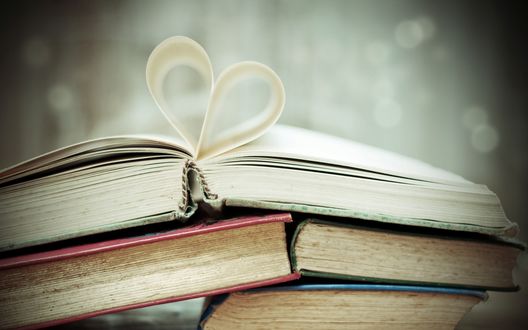 Обои на рабочий стол Стопка книг, у верхней открытой книги страницы загнуты в форме сердца