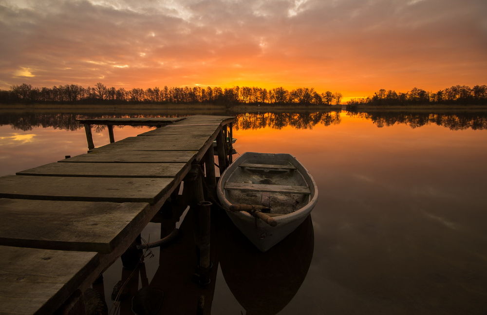 Обои для рабочего стола Лодка, стоящая на озере у деревянной пристани на фоне заката на вечернем небосклоне