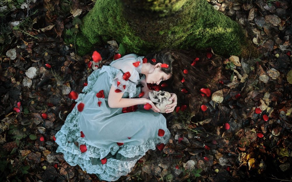 Обои для рабочего стола Девушка, усыпанная лепестками роз, лежит на земле и разговаривает с черепом, который держит в руках