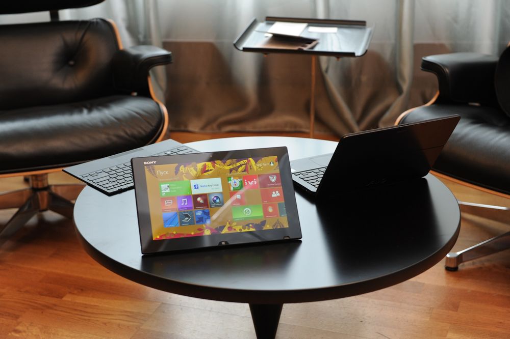 Обои для рабочего стола Планшет фирмы Sony / Сони на столе, с установленным программным обеспечением Windows / Виндоус, рядом стоит ноутбук