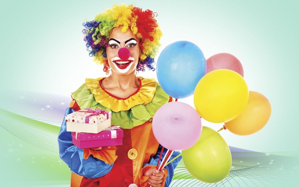 Обои для рабочего стола Девушка в костюме клоуна стоит с разноцветными воздушными шариками и с подарками в руках