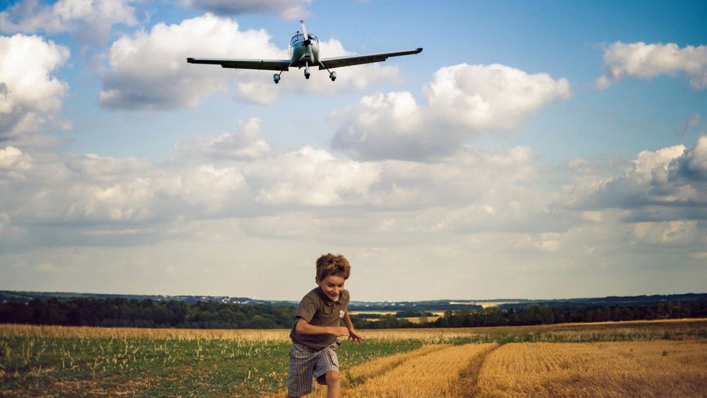 Обои для рабочего стола Над полем пролетает самолет, от которого убегает мальчик