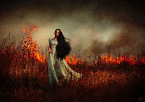 Обои на рабочий стол Стройная, черноволосая девушка в длинном, бирюзовом платье, стоящая на фоне сухой, горящей травы с клубами дыма, поднимающегося к небу, автор Светлана Беляева