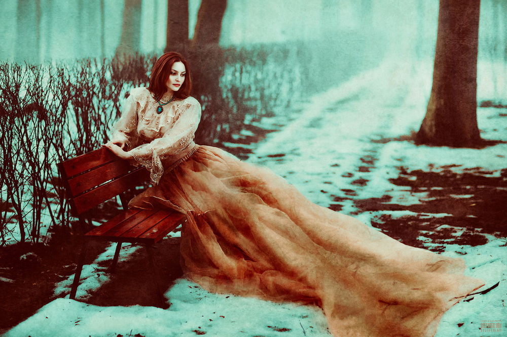 Обои для рабочего стола Красивая, рыжеволосая женщина в длинной, пышной юбке, сидящая на скамейке, расположенной на аллее парка, припорошенной свежевыпавшим снегом с легкой туманной дымкой, автор Светлана Беляева