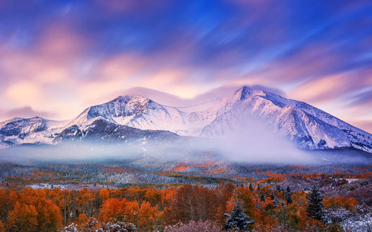 Обои на рабочий стол Деревья с яркой окраской, покрытые инеем, в легком тумане на фоне заснеженных гор освещенных лучами восходящего солнца