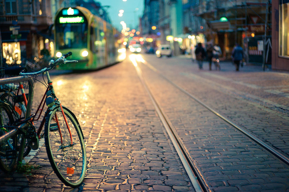Обои для рабочего стола На переднем плане стоит велосипед перед трамвайными путями, где виден трамвай и в стороне улицы идут люди, фотограф Oleg Bagmutskiy