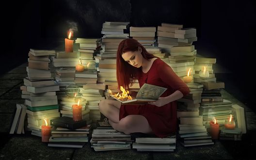 Обои на рабочий стол Девушка сидит в окружении книг и зажженных свечей и сжигает книгу