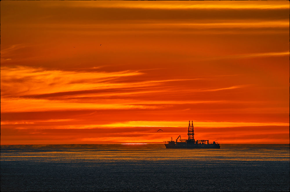 Обои для рабочего стола Грузовая баржа, плывущая по морю на фоне вечернего небосклона с разноцветными облаками
