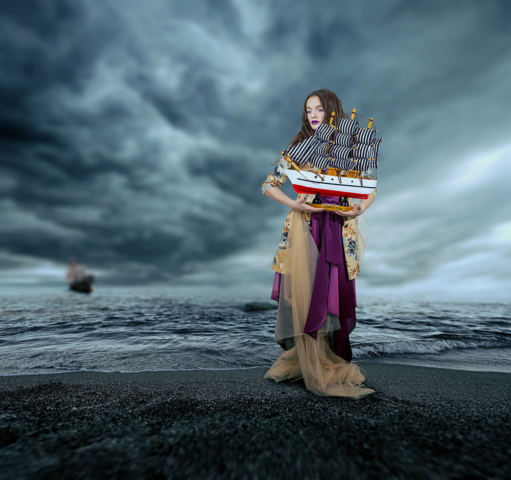 Обои для рабочего стола Темноволосая девушка, держащая в руке макет парусника, стоящая на морском побережье на фоне уплывающего парусного фрегата в туманную мглу, автор Garas Ionut
