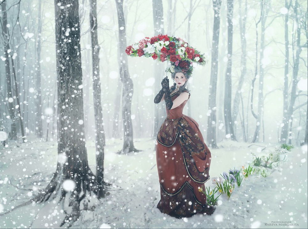 Обои для рабочего стола Темноволосая девушка в легком платье, стоящая на опушке под падающими снегом, держащая в руках зонтик, усыпанный цветами, автор Маргарита Карева