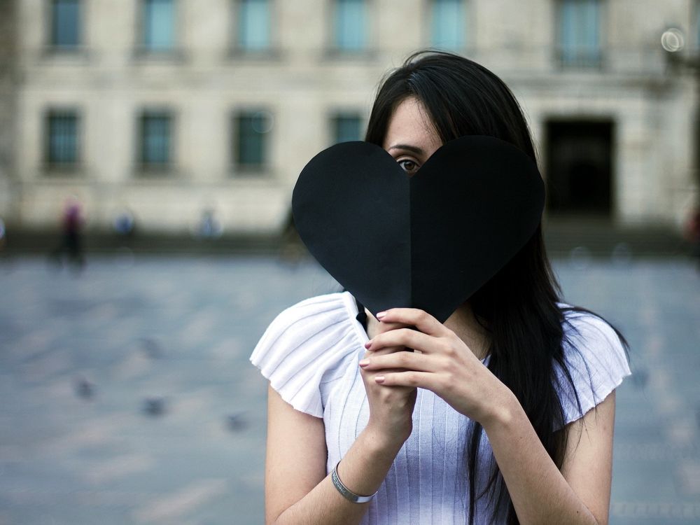 Обои для рабочего стола Девушка прикрывает лицо черным бумажным сердцем