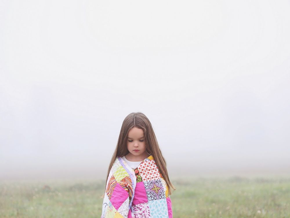Обои для рабочего стола Девочка стоит посреди поля, укрытого туманом, закутавшись в плед