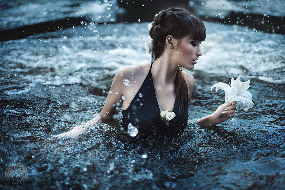 Обои для рабочего стола Темноволосая девушка в черном платье, стоящая в прибрежной морской воде, держащая в руке белый цветок, автор Марина Бабинцева