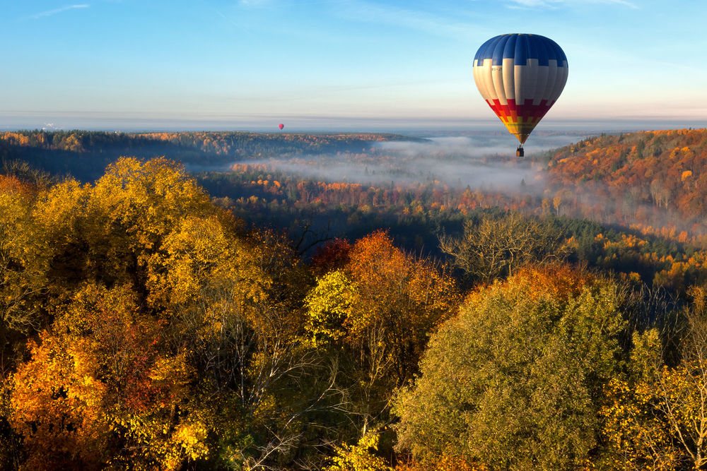 Обои для рабочего стола Воздушный шар, парящий в небе над лощиной между холмами, покрытыми деревьями с осенней листвой и легкой туманной дымкой