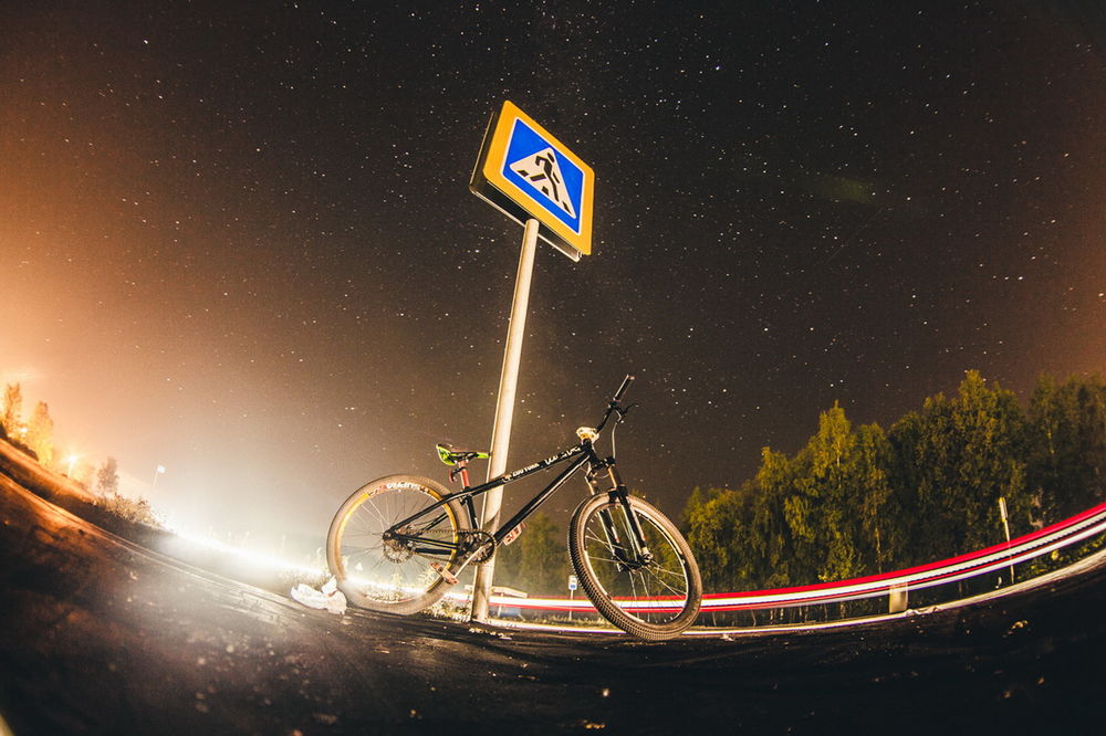 Обои для рабочего стола Велосипед, стоящий у дорожного знака на фоне звездного, ночного неба
