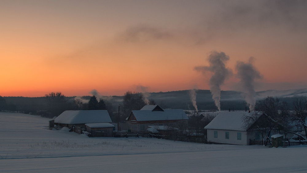 Обои для рабочего стола Окраина деревни, занесенная снегом с выходящим из печных труб домов белым дымом на рассвете