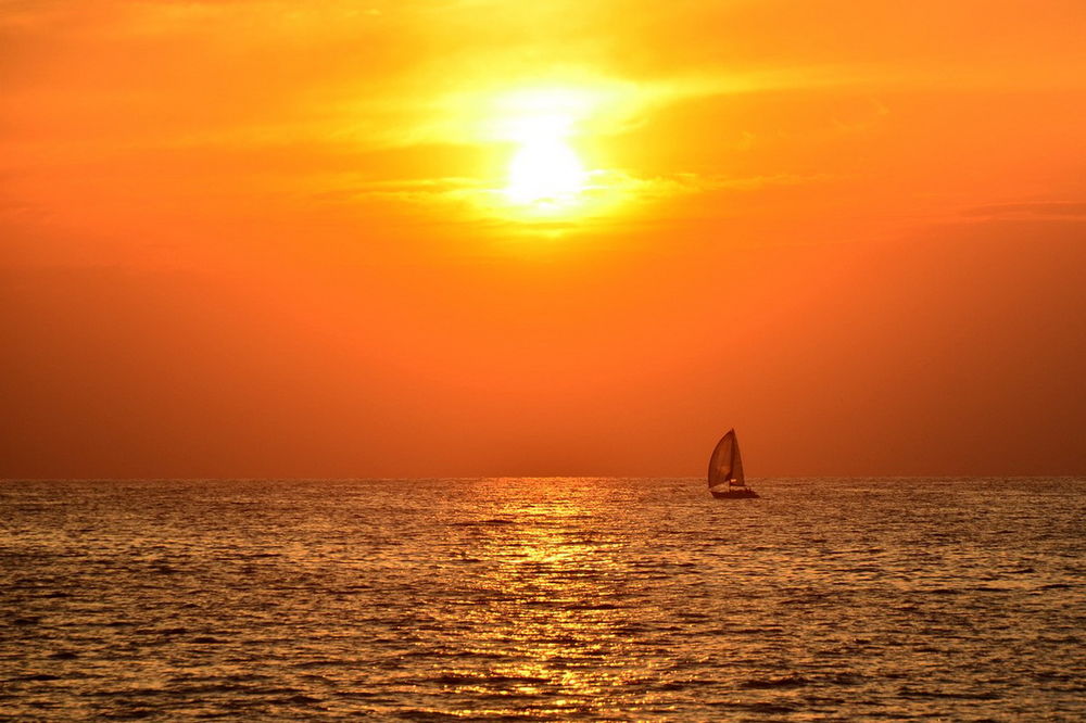 Обои для рабочего стола Парусник, плывущий по морю на фоне золотистых лучей заходящего солнца на вечернем небосклоне