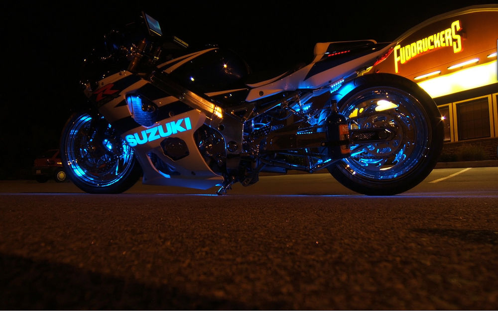 Обои для рабочего стола Мотоцикл SUZUKI с синей неоновой посветкой стоит на асфальте, возле здания