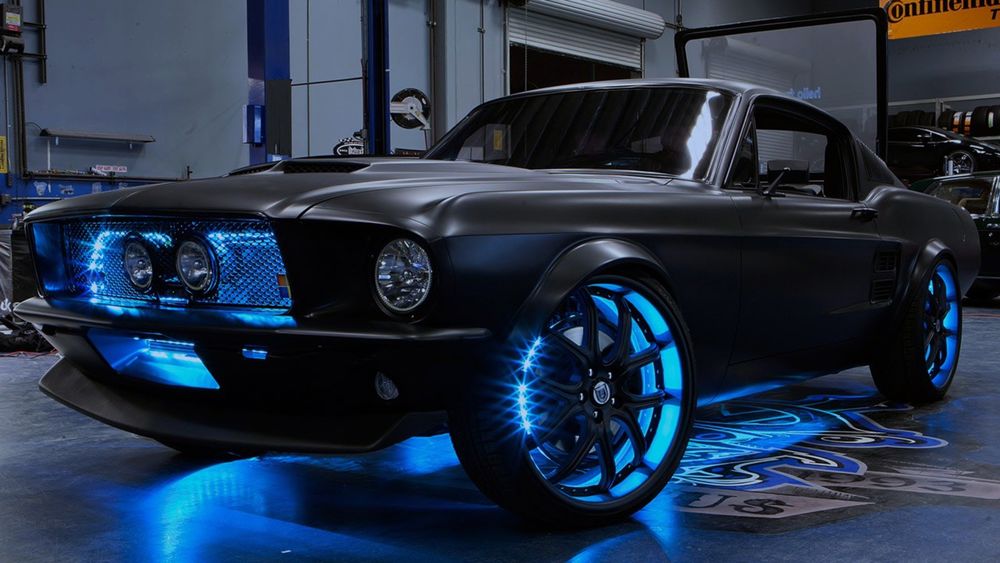 Обои для рабочего стола Черный легковой автомобиль марки BMW, стоит в гараже с включенной голубой неоновой подсветкой в колесах и передней панели
