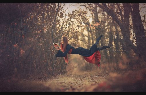 Обои на рабочий стол Рыжеволосая девушка, читающая книгу, парящая над землей на опушке леса, автор Виталий Здрок
