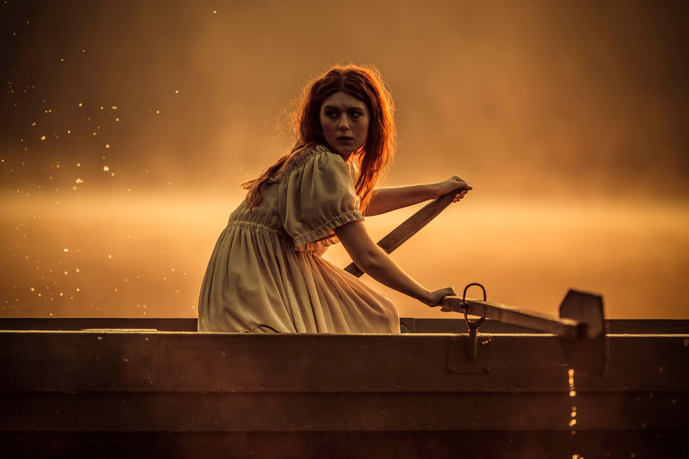 Обои для рабочего стола Рыжеволосая девушка, сидящая за веслами в лодке, настороженно вглядывается в туманную мглу над рекой