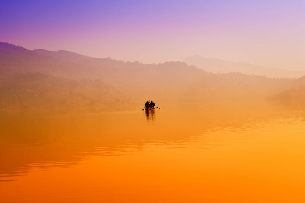 Обои для рабочего стола Мужчины, сидящие в лодке с веслами в руках, плывущие в утреннем, желтом тумане на озере, невдалеке от холмистого берега на рассвете
