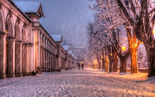 Обои на рабочий стол Ночные улицы города под падающим снегом, деревьями и ярко горящими фонарями по обочине, идущими под зонтиками людьми